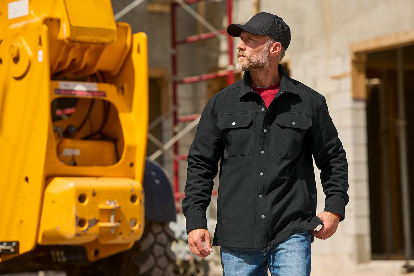 Man in a black jacket and cap standing next to a yellow piece of construction equipment. CornerStone® Soft Shell Shirt Jacket, Embroidered