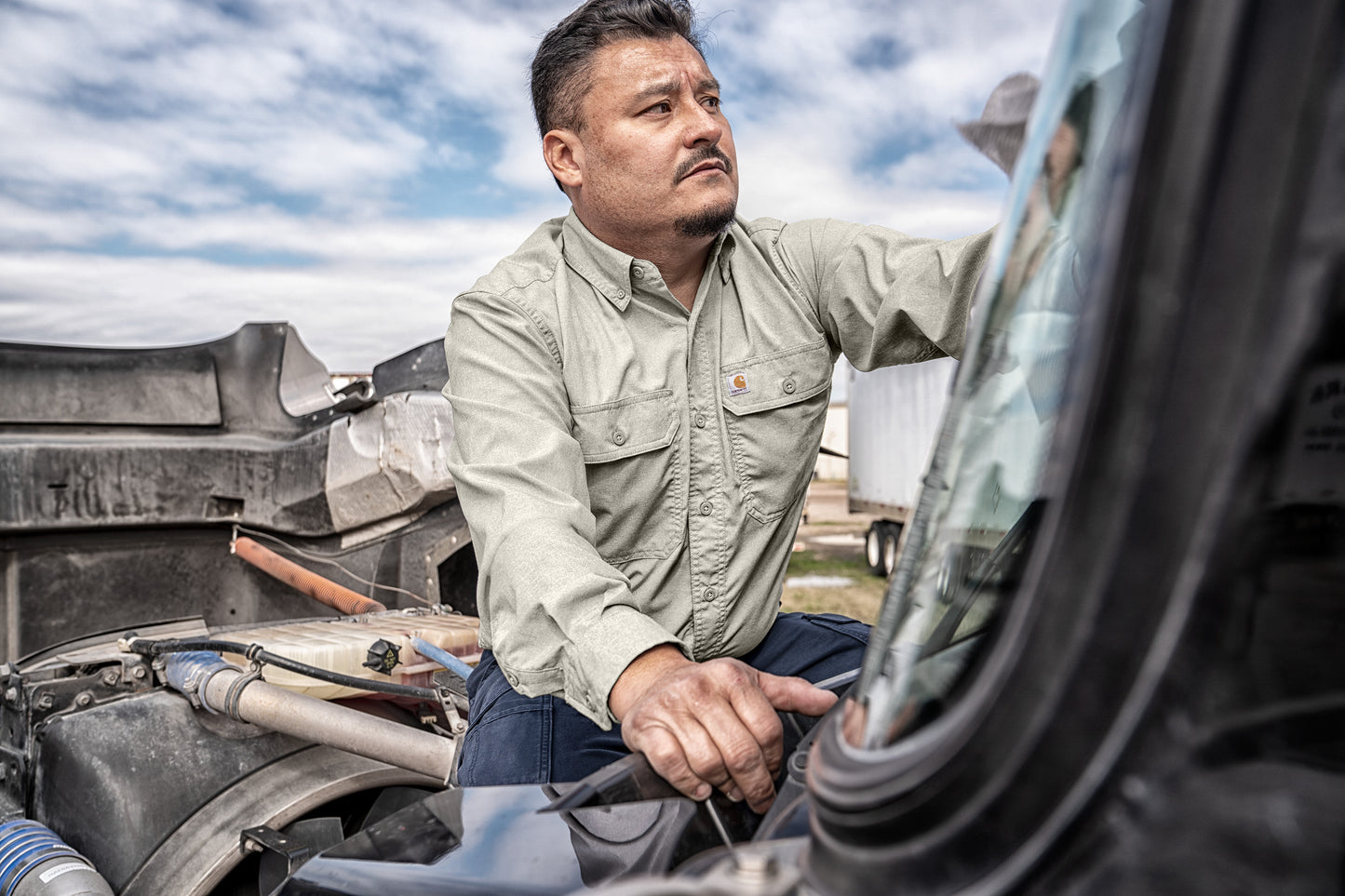 Man working on a vehicle with a clear sky background embroidered Carhartt Force® Solid Long Sleeve Shirt