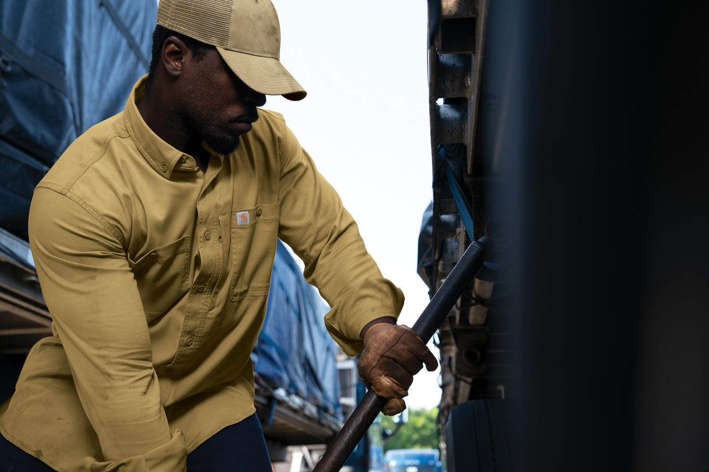 Person in beige work shirt and cap working on a vehicle embroidered Carhartt® Rugged Professional™ Series Long Sleeve Shirt