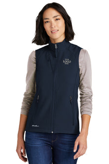 Woman wearing a navy blue vest with a logo on a white background embroidered Eddie Bauer® Women's Stretch Soft Shell Vest