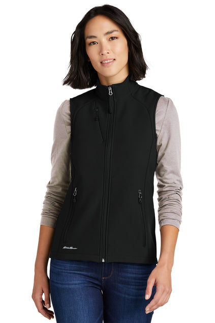 Woman wearing a black vest over a gray long-sleeve shirt on a white background embroidered Eddie Bauer® Women's Stretch Soft Shell Vest