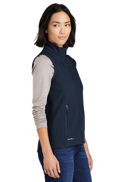 Woman wearing a navy blue vest over a light gray shirt on a white background embroidered Eddie Bauer® Women's Stretch Soft Shell Vest