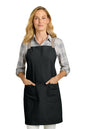 A woman modeling a black bib apron with beige shoulder straps over a gray and white plaid button-down shirt, set against a solid white background. Port Authority® Signature Heavy Twill Crossback Apron, Embroidered