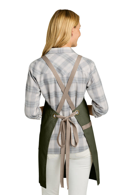 Woman wearing a green apron with beige straps on a white background. Port Authority® Signature Heavy Twill Crossback Apron, Embroidered