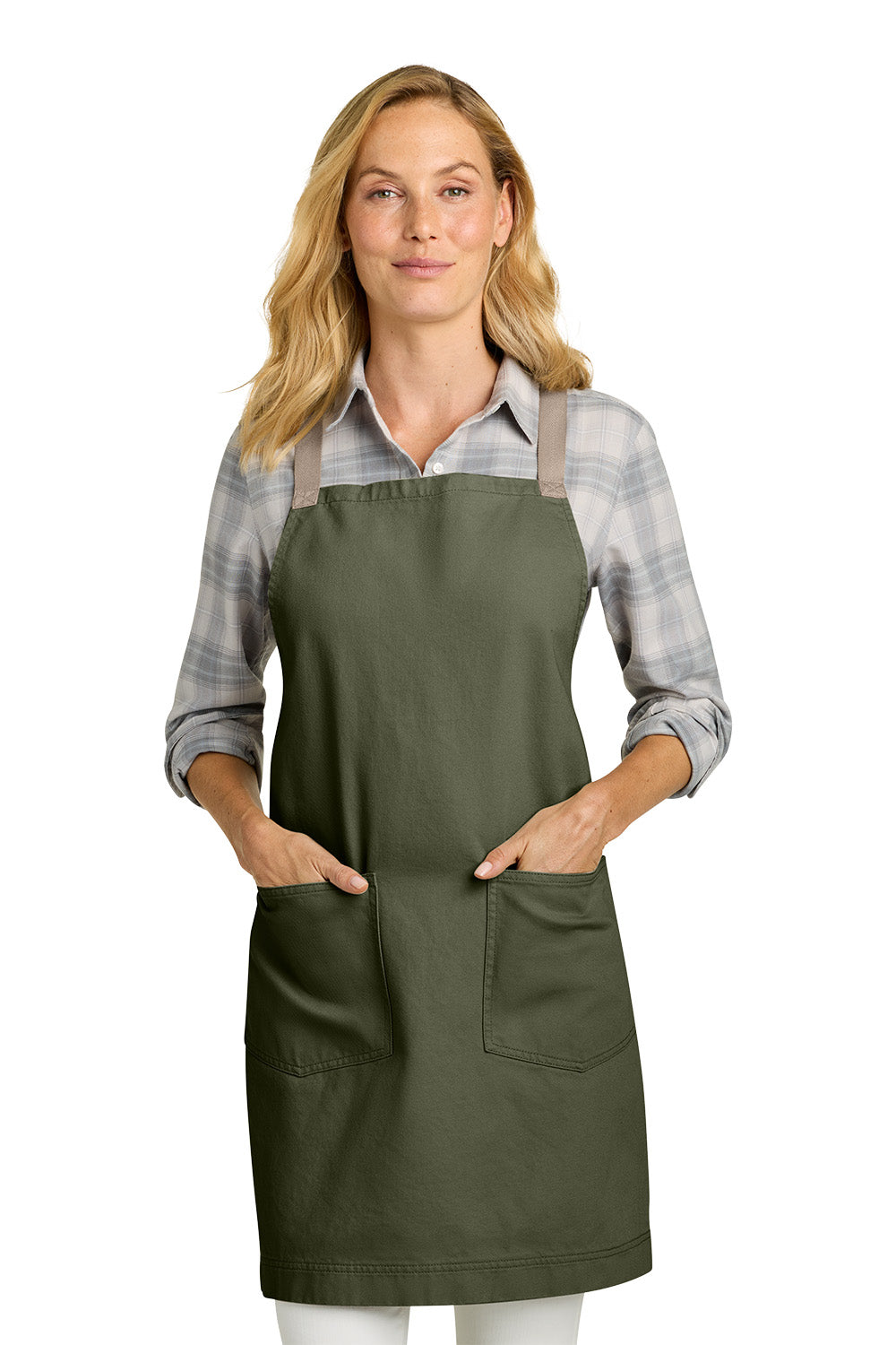 A woman wearing an olive green bib apron with two front pockets over a gray and white plaid button-down shirt, photographed against a solid white background. Port Authority® Signature Heavy Twill Crossback Apron, Embroidered