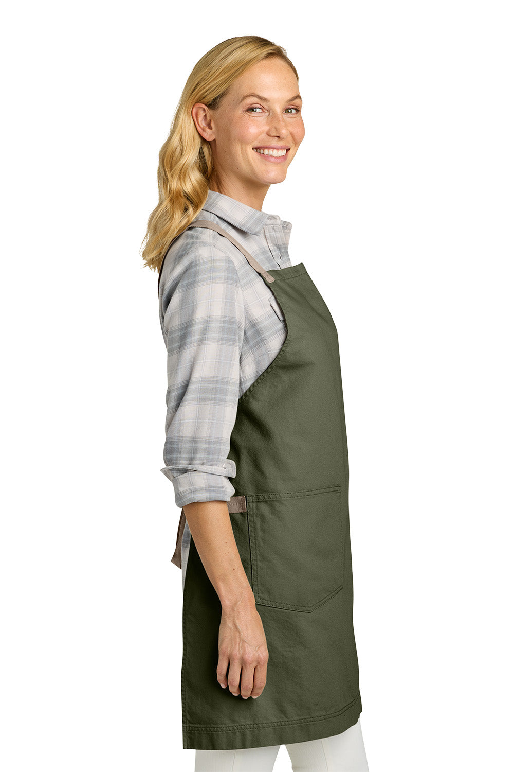 A woman wearing an olive green bib apron over a gray and white plaid flannel shirt, shown from a side profile against a solid white background. Port Authority® Signature Heavy Twill Crossback Apron, Embroidered