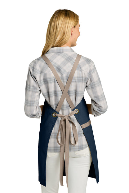 Woman wearing a blue apron with beige straps on a white background. Port Authority® Signature Heavy Twill Crossback Apron, Embroidered