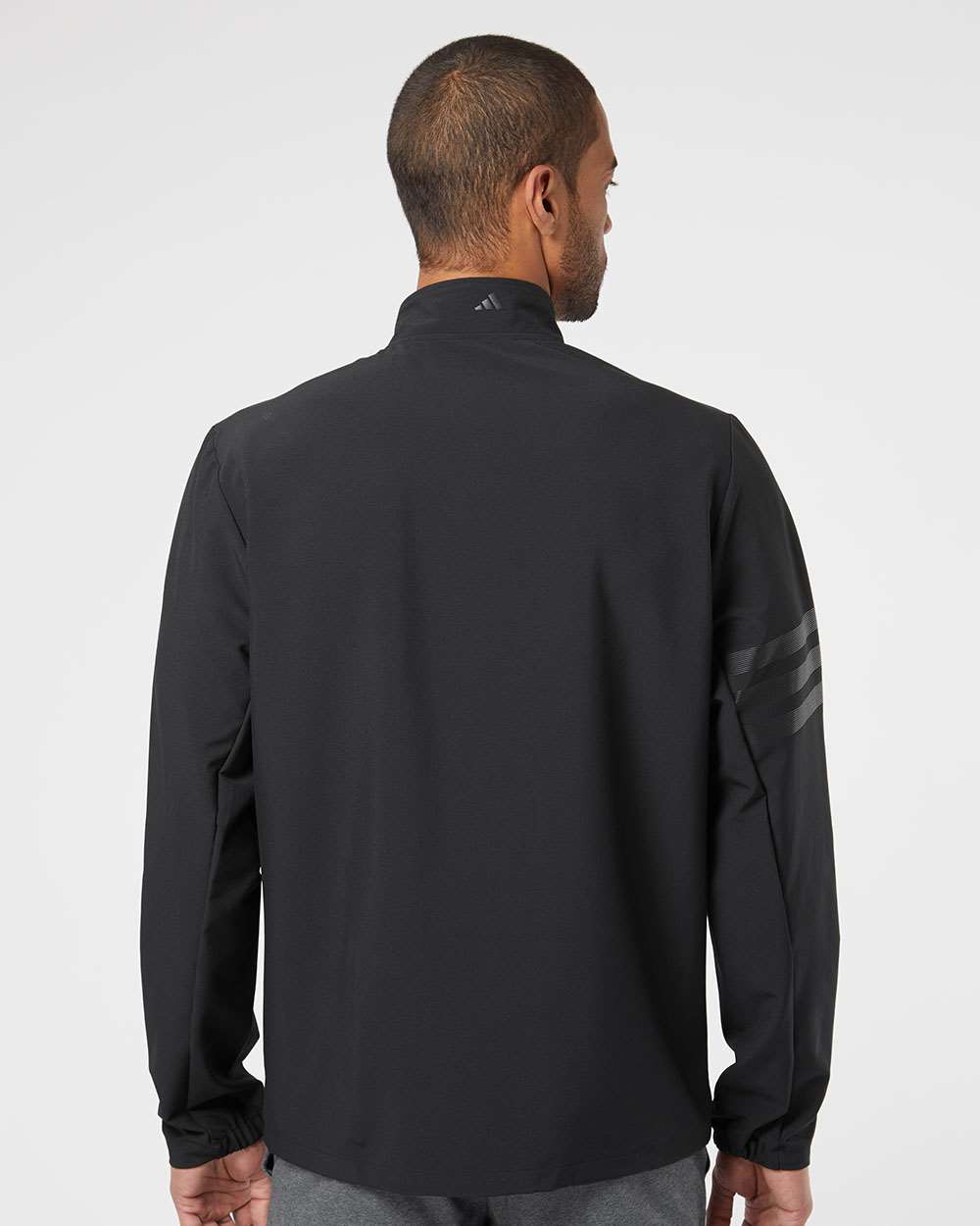 Man wearing a black jacket with a brand logo on the sleeve against a white background. Adidas Men's Wind Resistant Full-Zip Jacket, Embroidered by Helmsman Stitch Co.