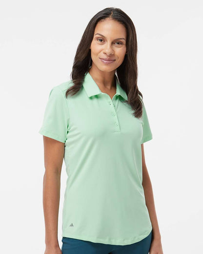 Woman wearing a light green polo shirt on a white background. Adidas Women's Ultimate365 Solid Polo, Embroidered by Helmsman Stitch Co.