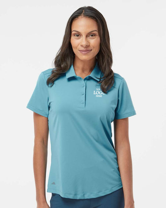 Woman wearing a teal polo shirt with a logo on a white background. Adidas Women's Ultimate365 Solid Polo, Embroidered by Helmsman Stitch Co.