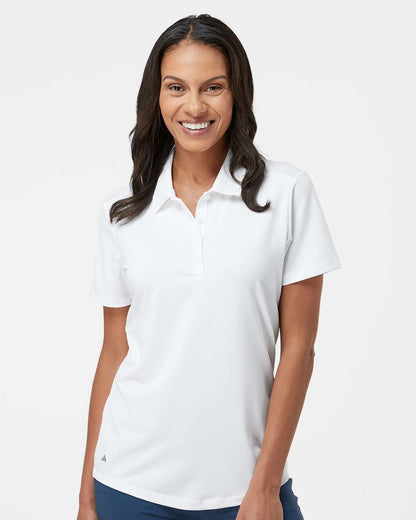 Woman wearing a white polo shirt on a plain background. Adidas Women's Ultimate365 Solid Polo, Embroidered by Helmsman Stitch Co.