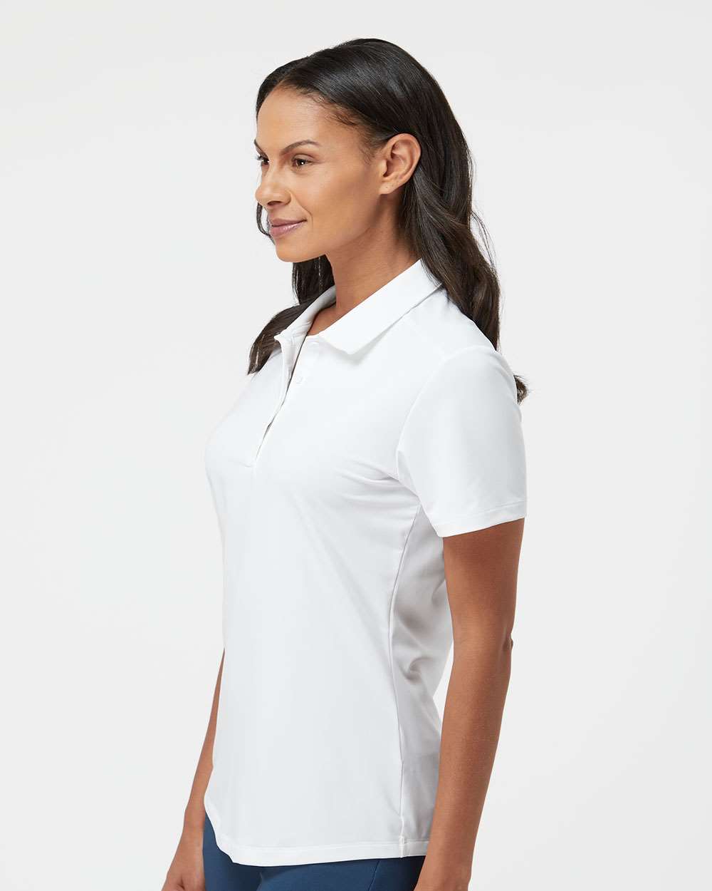 Woman wearing a white polo shirt on a light gray background. Adidas Women's Ultimate365 Solid Polo, Embroidered by Helmsman Stitch Co.