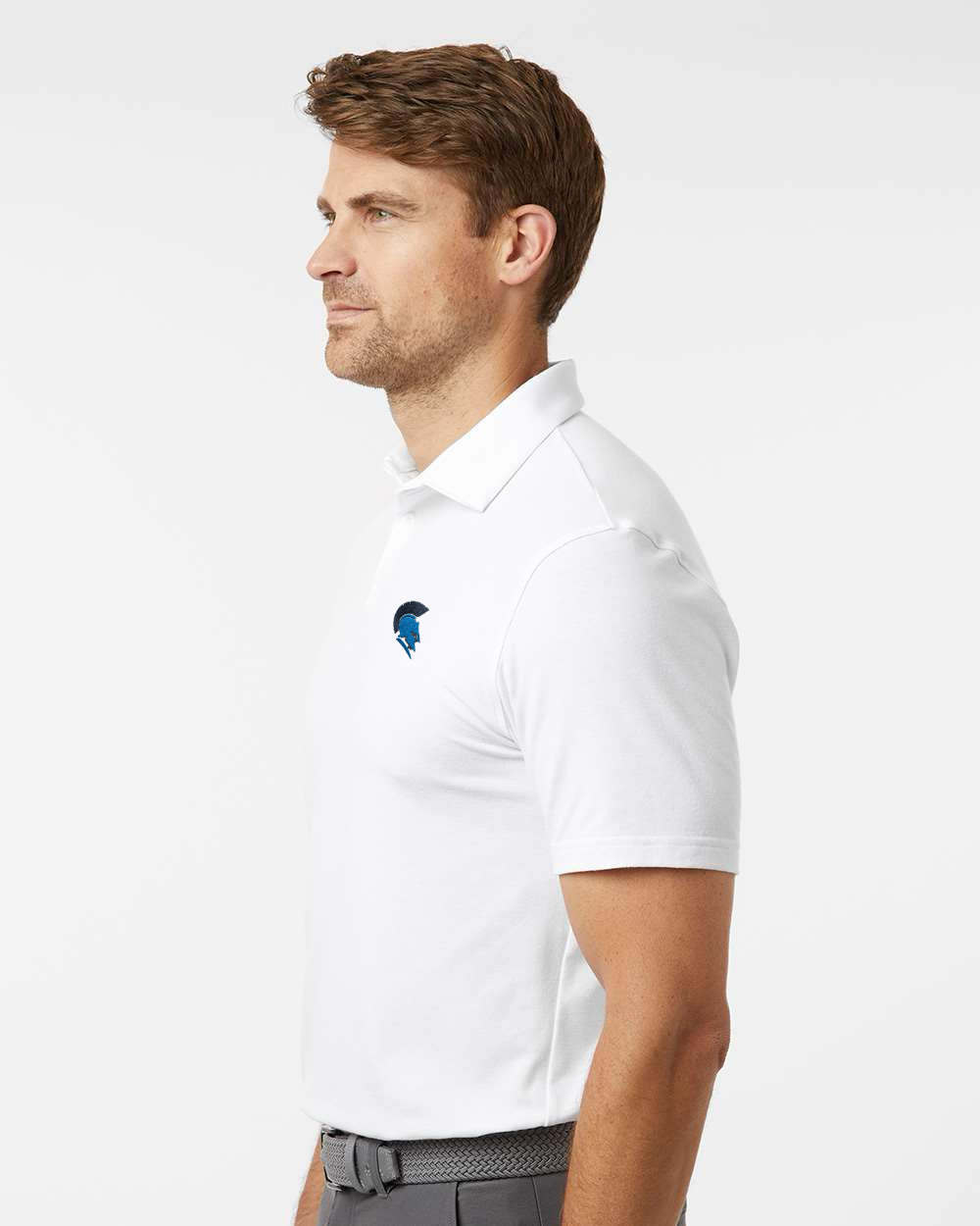 Man wearing a white polo shirt with a logo on a light gray background. Adidas Men's Blended Polo, Sparta Michigan Spartans logo by Helmsman Stitch Co.