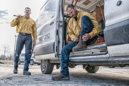 Two men in yellow jackets and jeans standing next to a van, with one man sitting inside the van. embroidered Carhartt Force® Solid Long Sleeve Shirt