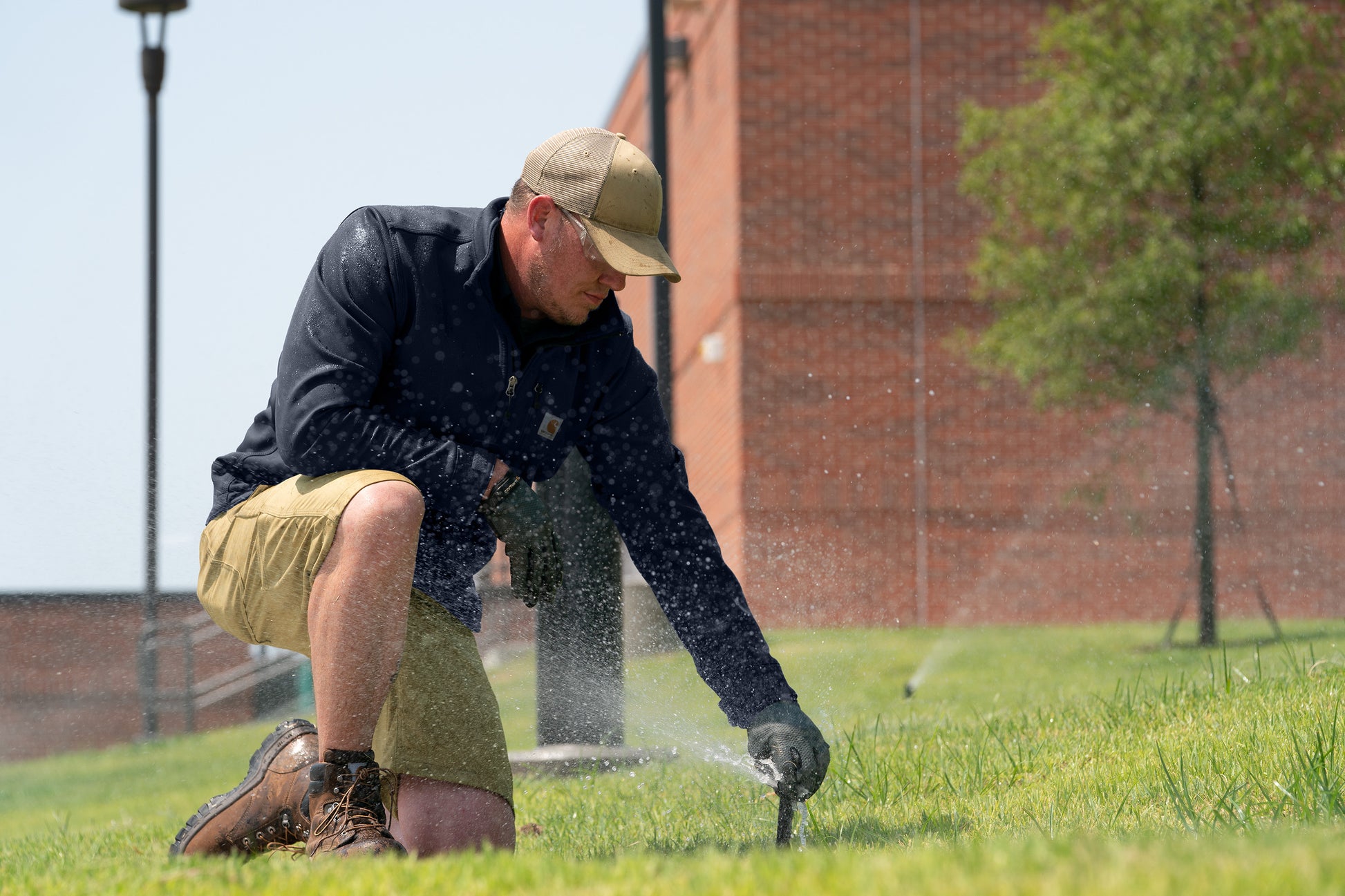 Person using a sprinkler to water grass in front of a brick building, Carhartt® Rugged Professional™ Series Cap, Embroidered