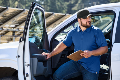 Man in a blue shirt and cap getting out of a white van with a clipboard. Carhartt® Rugged Professional™ Series Cap, Embroidered