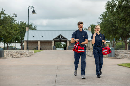 Two emergency responders walking outdoors with equipment bags.