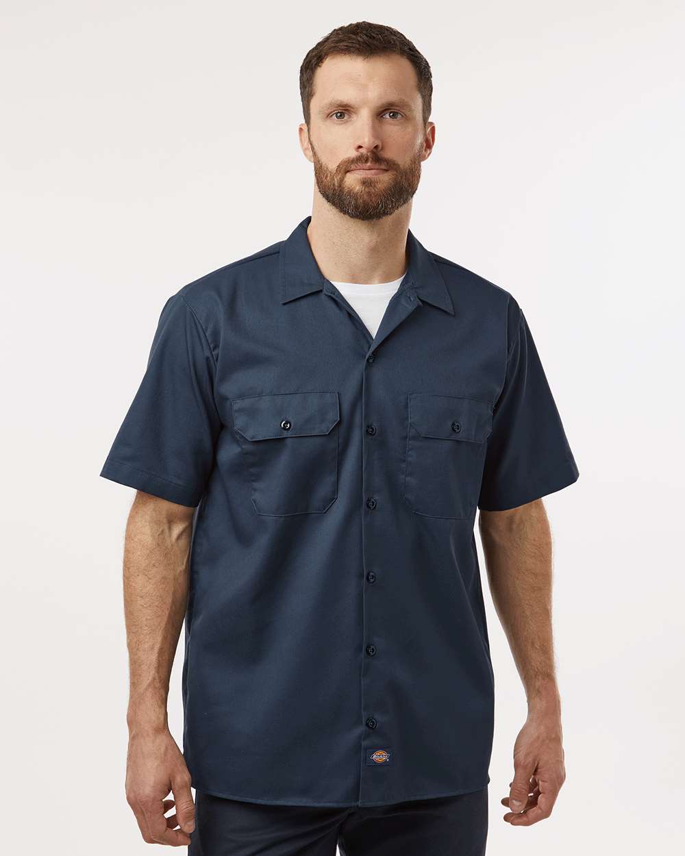 Man wearing a navy short-sleeve shirt on a white background. Dickie's Men's Shirt Sleeve Work Shirt, Embroidered by Helmsman Stitch Co.