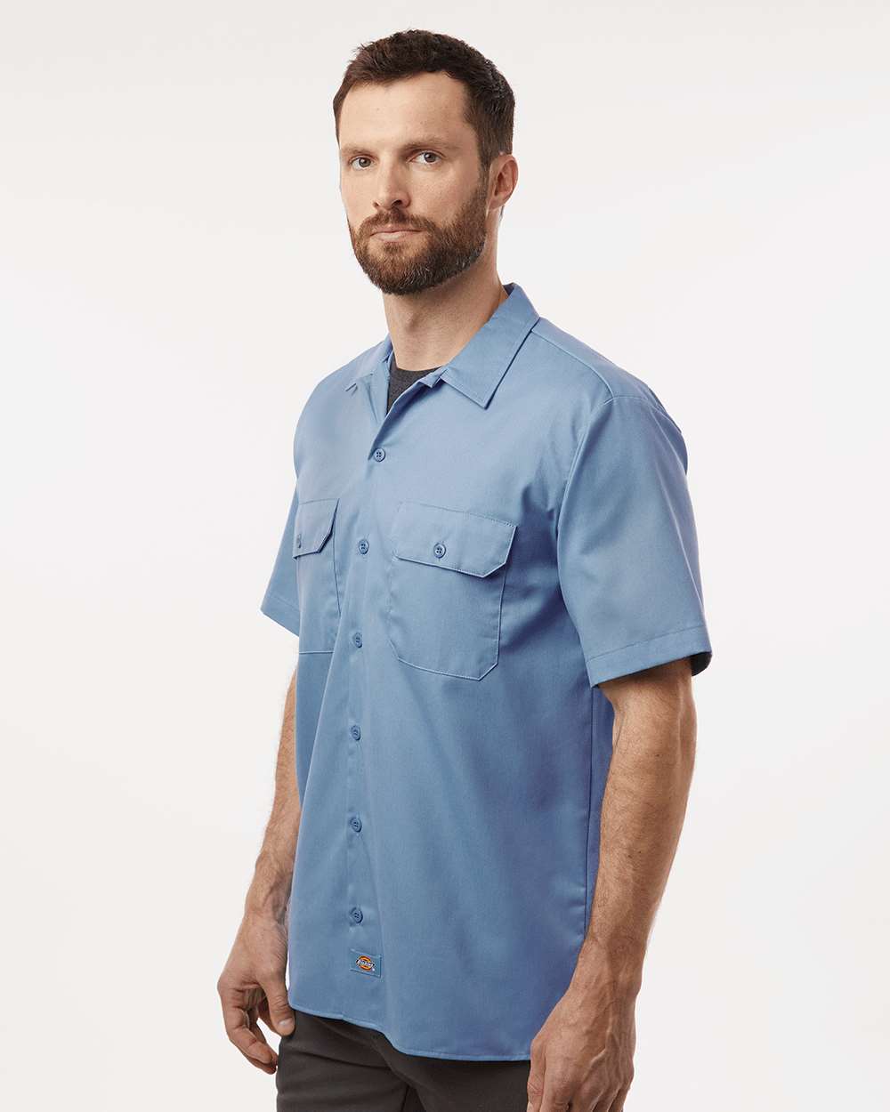 Man wearing a light blue short-sleeve shirt on a white background. Dickie's Men's Shirt Sleeve Work Shirt, Embroidered by Helmsman Stitch Co.