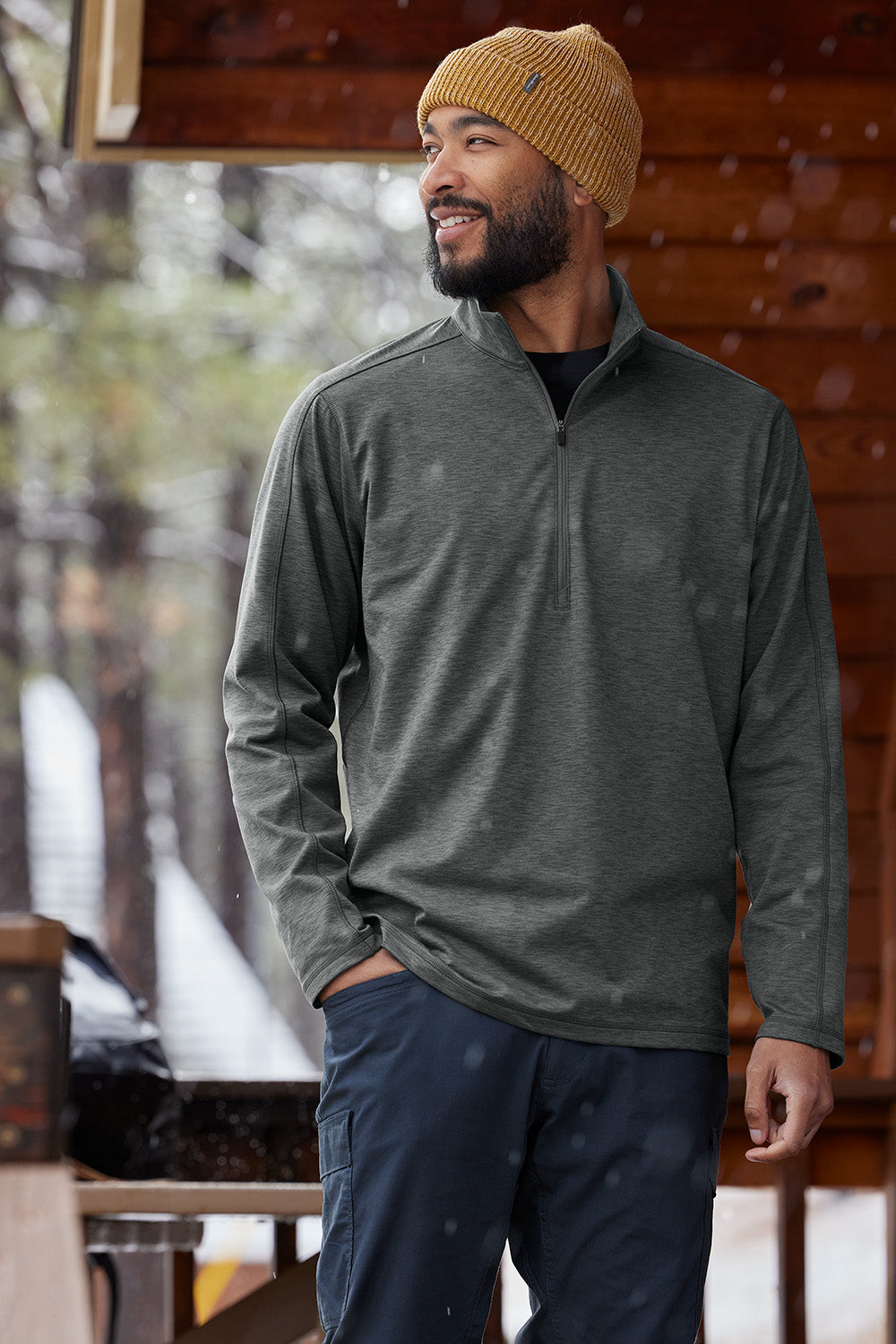 Man wearing a gray pullover and navy pants standing outdoors in a snowy setting. Eddie Bauer® Adventurer 1/4-Zip, Embroidered