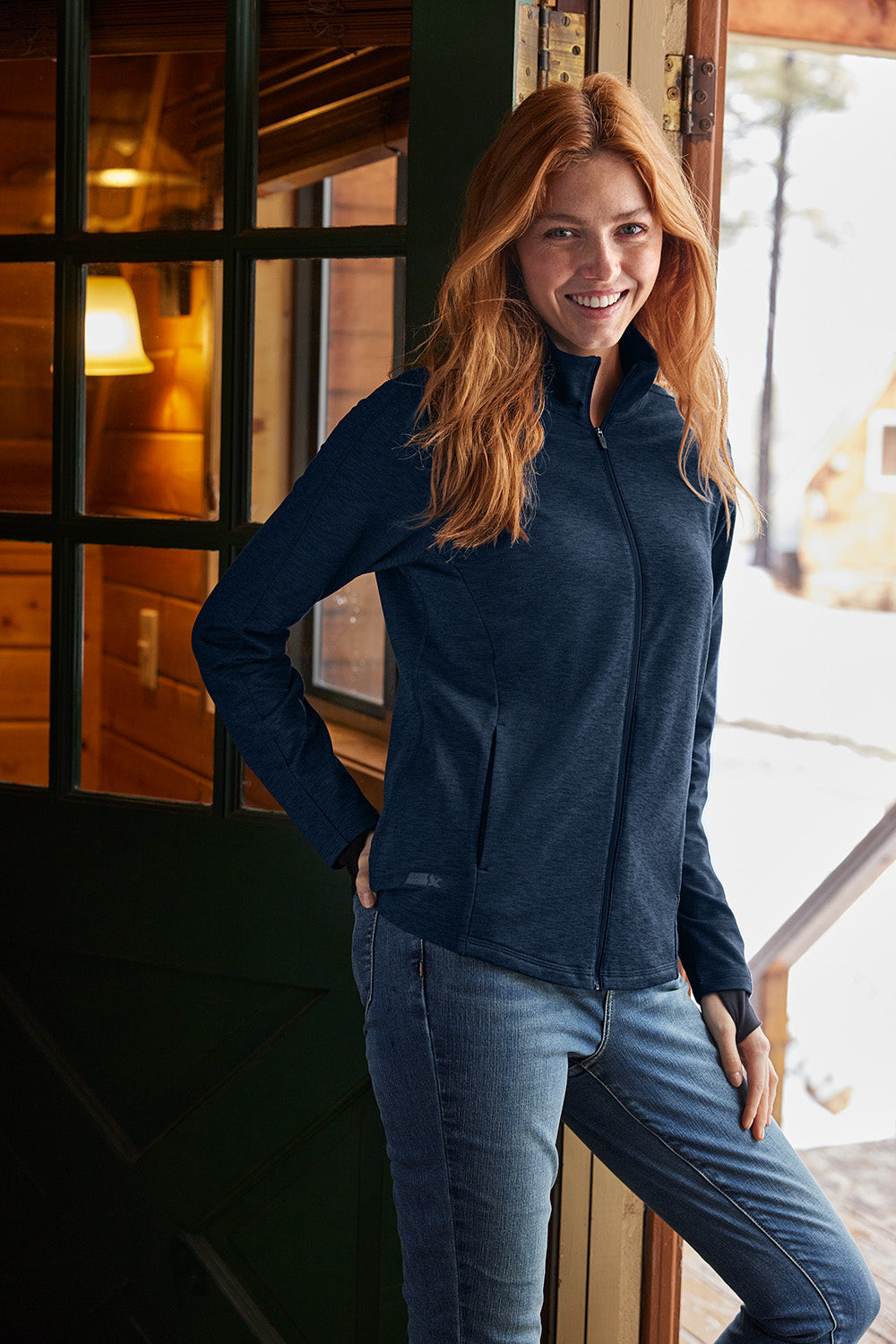 Woman wearing a navy jacket and blue jeans standing indoors. Eddie Bauer® Women’s Adventurer Full-Zip, Embroidered