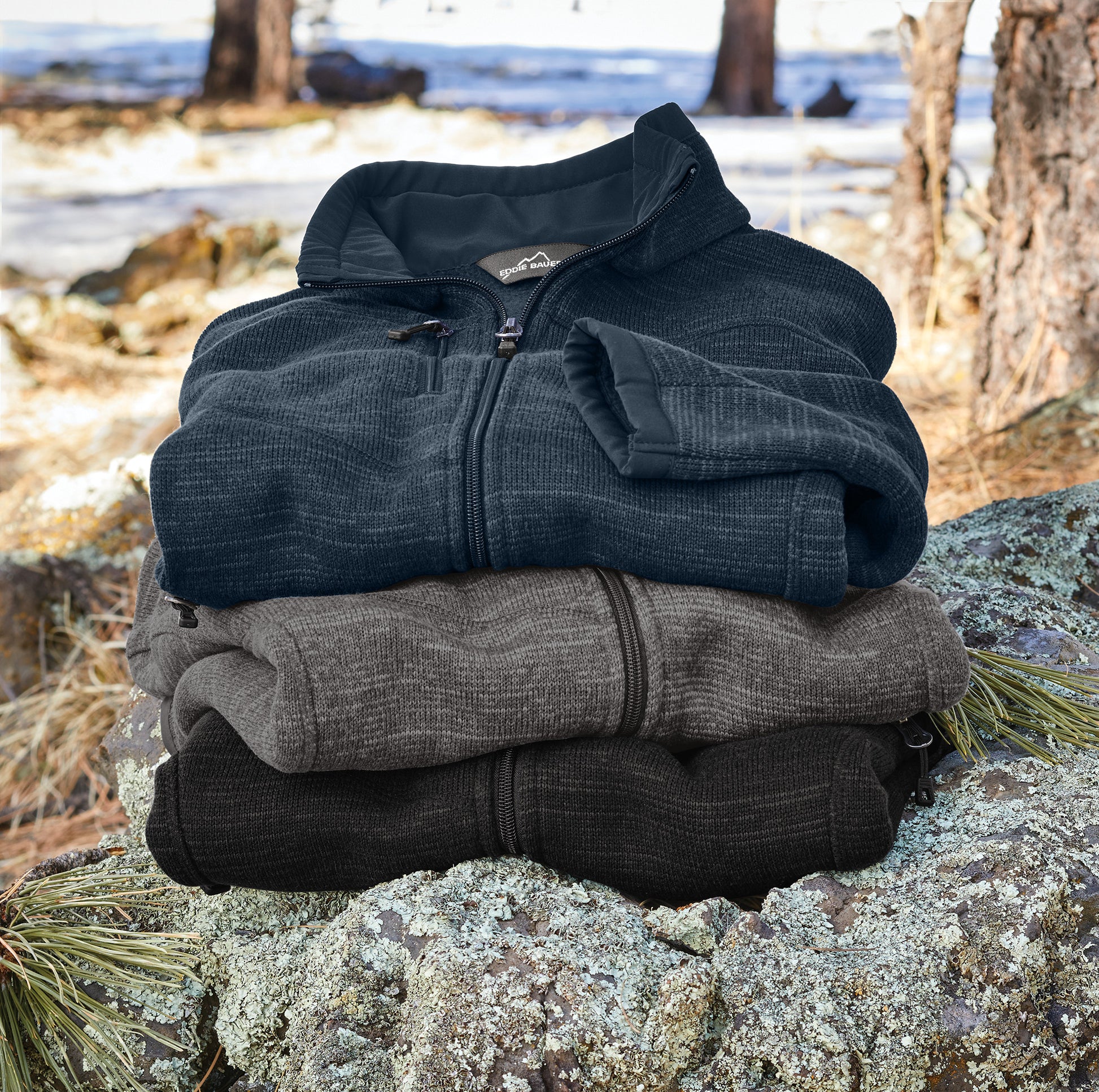 Stack of three jackets in black, gray, and blue on a rock with a forest background, Eddie Bauer® Sweater Fleece Full-Zip, Embroidered