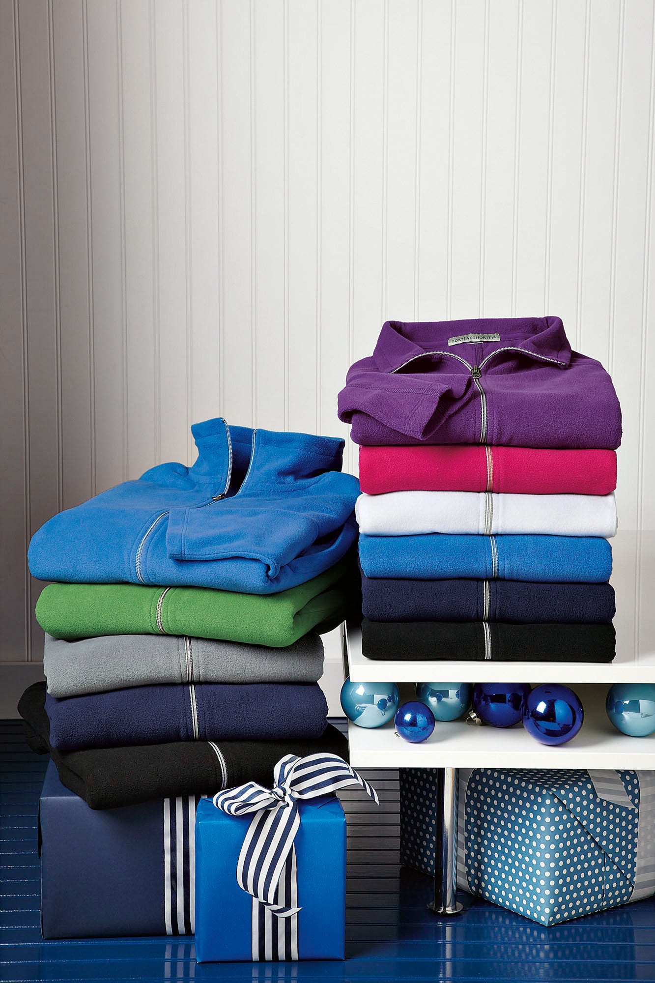 Stack of folded shirts in various colors on a white shelf with decorative items below. Port Authority® Women's Microfleece Jacket, Embroidered