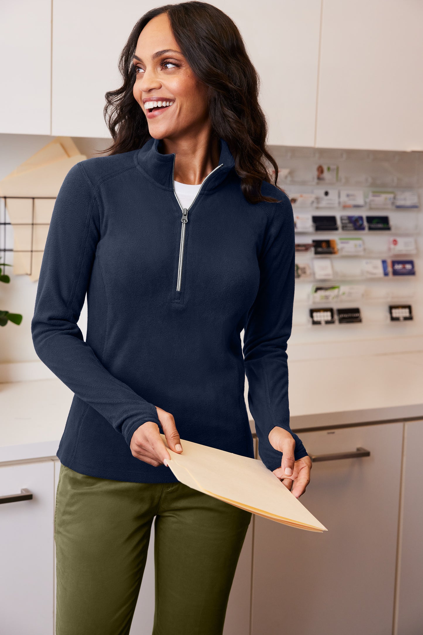 Woman wearing a navy long-sleeve shirt and green pants holding a wooden paddle in a kitchen. Port Authority® Women's Microfleece 1/2-Zip Pullover, Embroidered