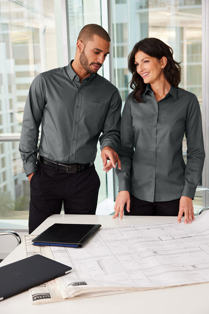 Two people in gray shirts looking at a tablet on a table with a modern office background. Port Authority® Women's SuperPro™ Twill Shirt, Embroidered