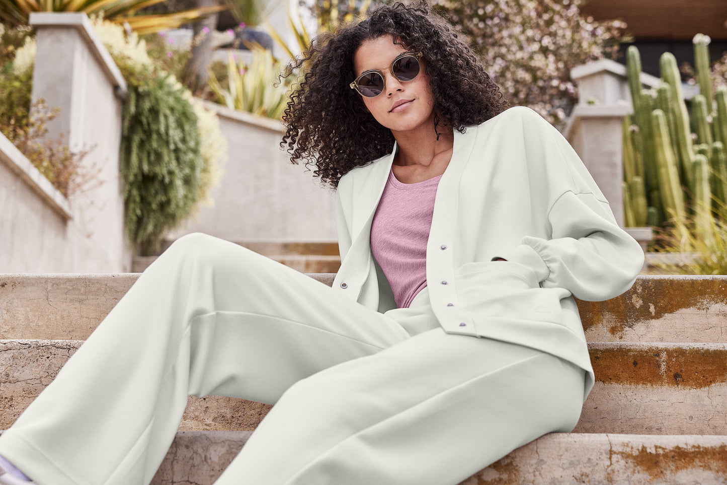 Woman in a light green outfit sitting on steps with plants in the background, OGIO® Women’s Transcend Cardigan, Embroidered