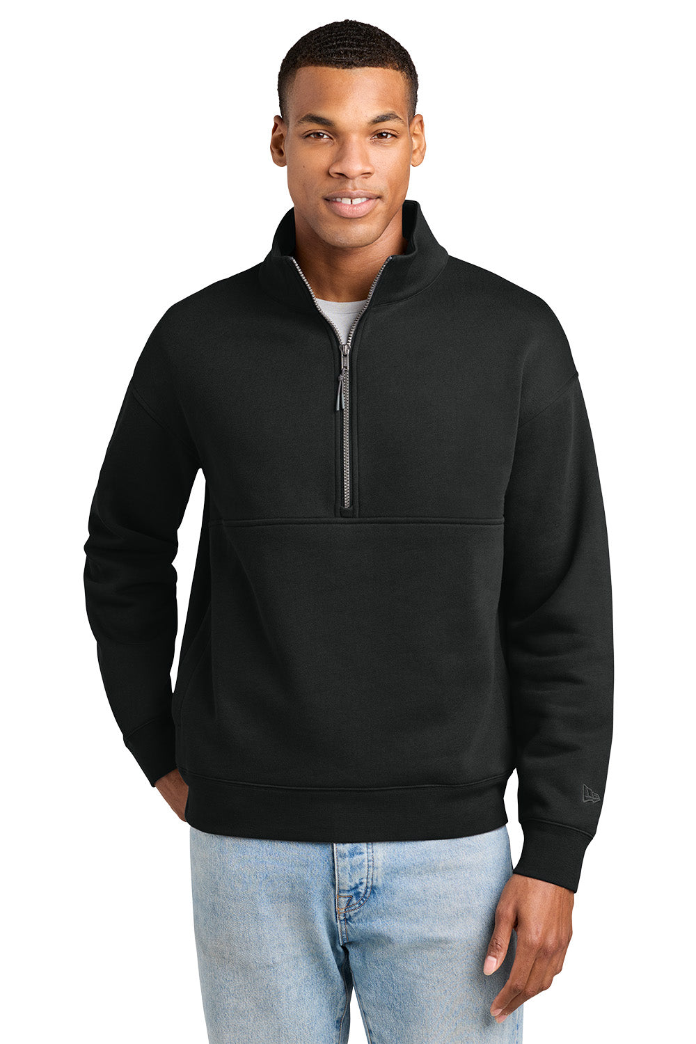 A man wearing a black quarter-zip pullover sweatshirt with a mock neck and a horizontal seam across the chest, paired with light blue jeans, against a plain white background. New Era® Heritage Fleece 1/2-Zip, Embroidered