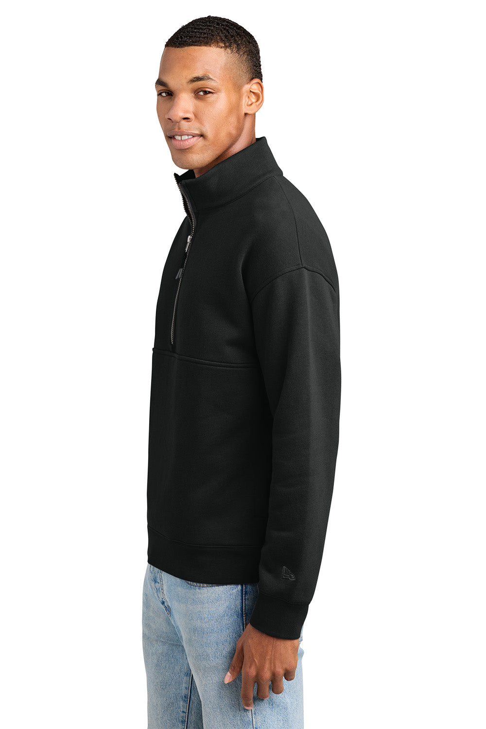 A man wearing a black quarter-zip pullover sweatshirt and light blue jeans, shown from a side profile against a plain white background. New Era® Heritage Fleece 1/2-Zip, Embroidered