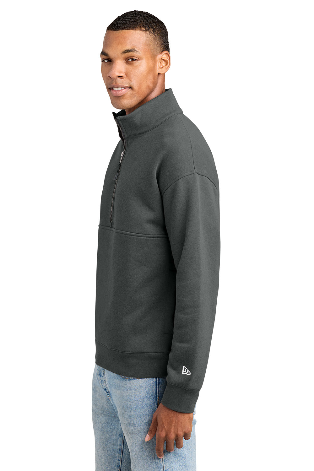 A man wearing a dark gray quarter-zip pullover sweatshirt with a small white New Era logo on the left sleeve cuff, paired with light blue jeans, shown against a plain white background. New Era® Heritage Fleece 1/2-Zip, Embroidered