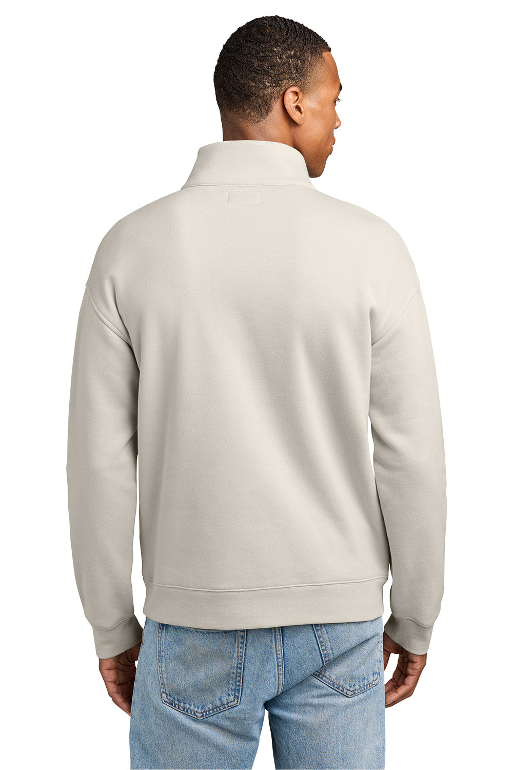 A man viewed from the back wearing a light beige quarter-zip sweatshirt and blue jeans against a plain white background. New Era® Heritage Fleece 1/2-Zip, Embroidered.