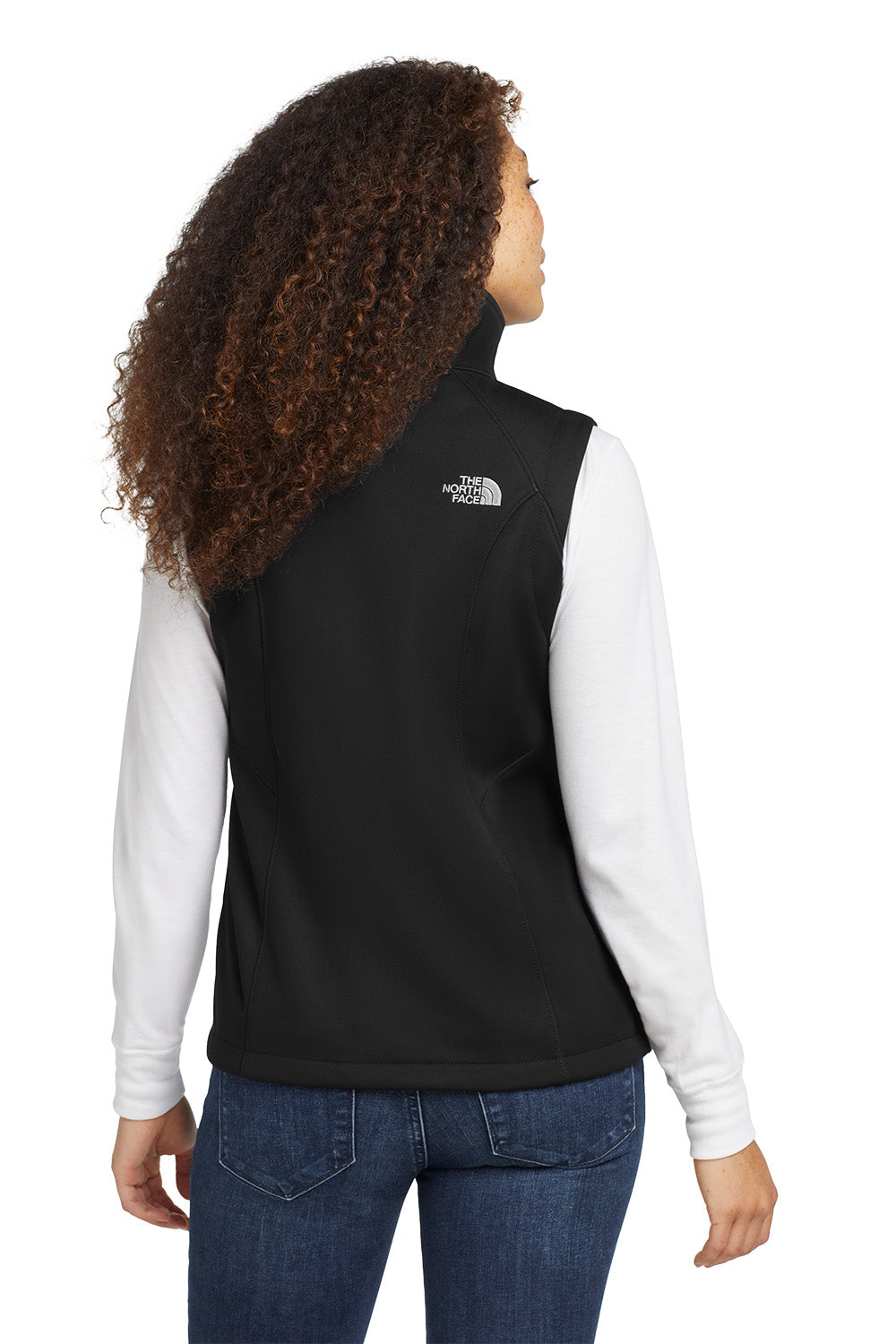 Person wearing a black vest with a logo on the back, white shirt, and blue jeans. embroidered The North Face® Women's Ridgewall Soft Shell Vest