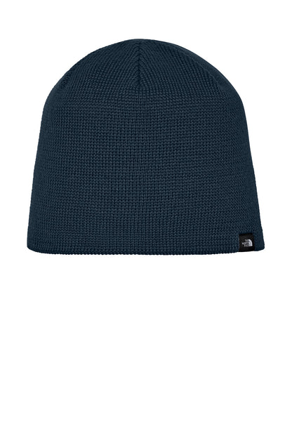 A dark navy blue ribbed knit beanie hat with a small black and white The North Face logo patch on the lower right side, shown against a plain white background. The North Face® Mountain Beanie, Embroidered