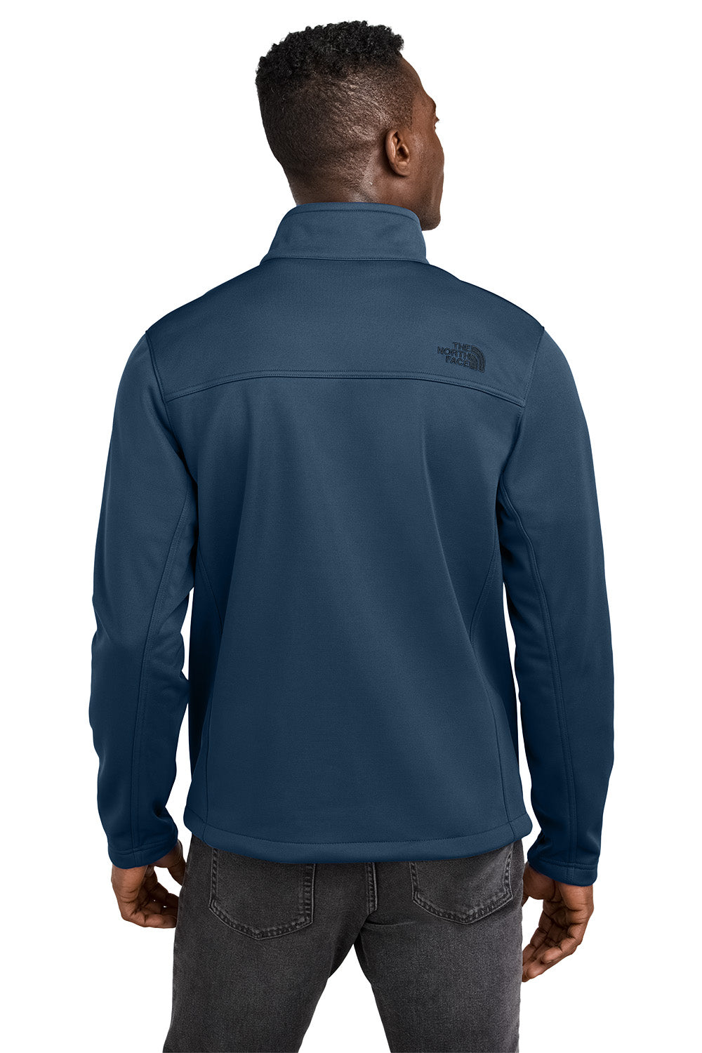 Person wearing a blue jacket with a visible brand logo on the back, standing against a white background. embroidered The North Face® Chest Logo Ridgewall Soft Shell Jacket