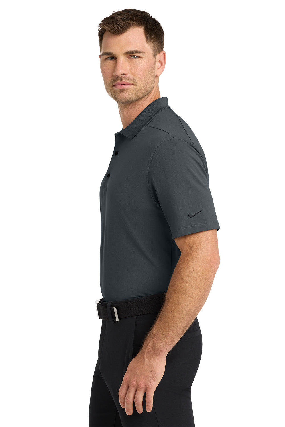 Man wearing a dark gray polo shirt and black pants on a white background. Nike Dri-FIT Micro Pique 2.0 Polo, Embroidered by Helmsman Stitch Co.