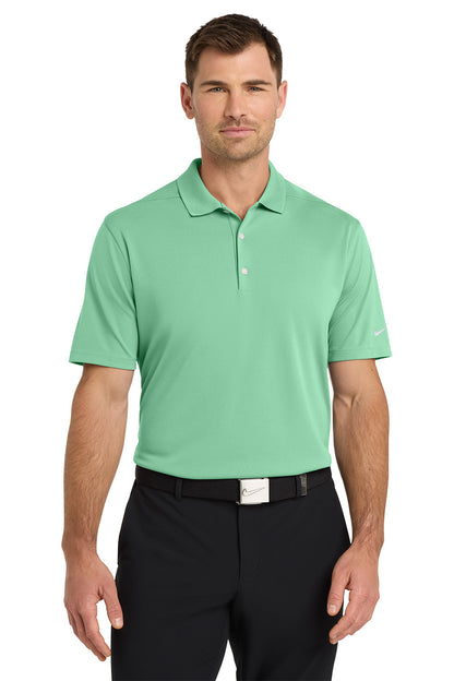 Man wearing a green polo shirt and black pants on a white background. Nike Dri-FIT Micro Pique 2.0 Polo, Embroidered by Helmsman Stitch Co.