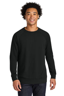 A man wearing a plain black long-sleeve crewneck sweatshirt, paired with dark blue jeans, standing against a solid white background. Next Level Apparel® Laguna Raglan Sweatshirt, Embroidered