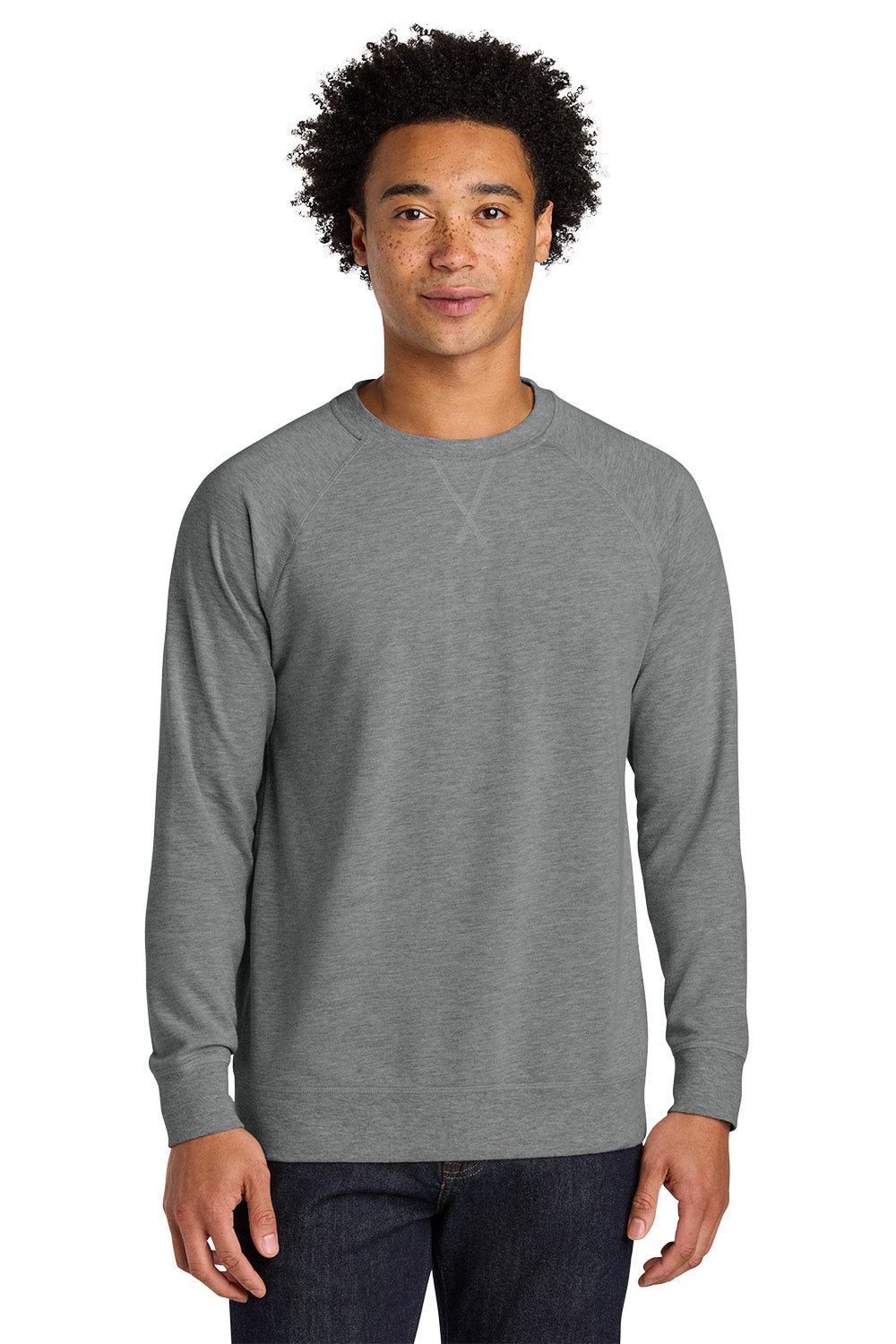 A man wearing a heather gray long-sleeve crewneck sweatshirt, paired with dark blue jeans, standing against a plain white background. Next Level Apparel® Laguna Raglan Sweatshirt, Embroidered