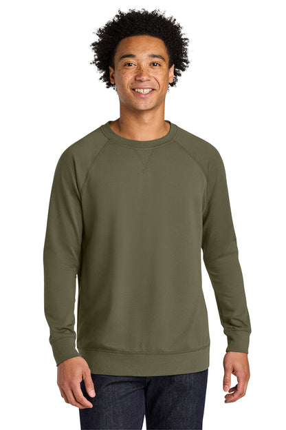 A man wearing an olive green long-sleeve crewneck sweatshirt, paired with dark blue jeans, standing against a plain white background. Next Level Apparel® Laguna Raglan Sweatshirt, Embroidered