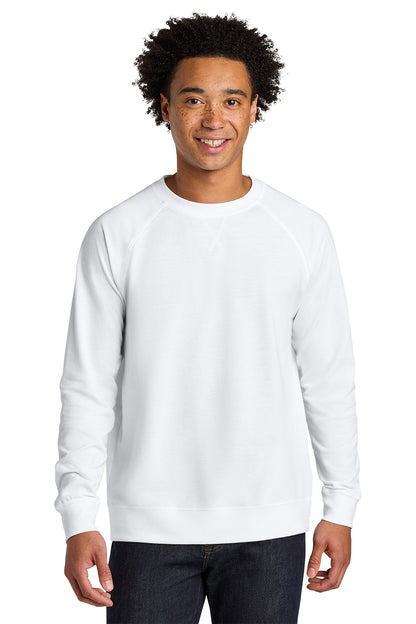 A smiling man with curly black hair wearing a plain white long-sleeve crewneck sweatshirt and dark blue jeans, standing against a solid white background. Next Level Apparel® Laguna Raglan Sweatshirt, Embroidered