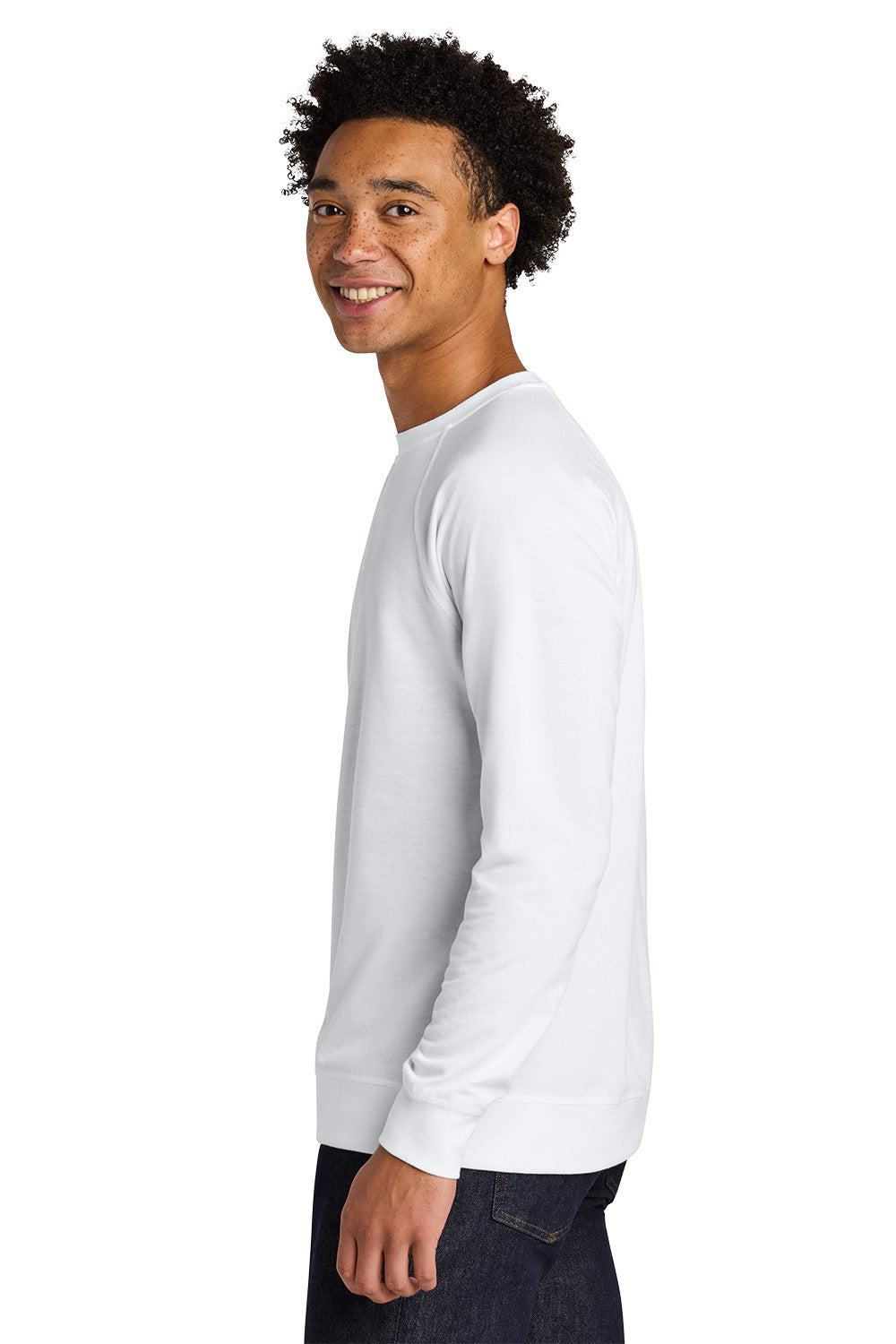 A man with curly black hair is shown in profile wearing a plain white long-sleeve crewneck shirt and dark jeans, photographed against a solid white background. Next Level Apparel® Laguna Raglan Sweatshirt, Embroidered