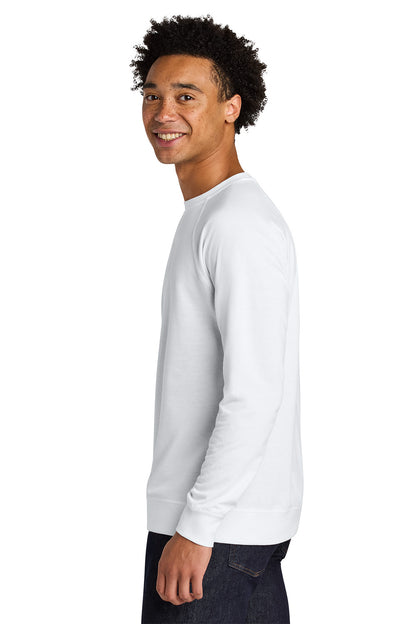 A man with curly black hair is shown in profile wearing a plain white long-sleeve crewneck shirt and dark jeans, photographed against a solid white background. Next Level Apparel® Laguna Raglan Sweatshirt, Embroidered