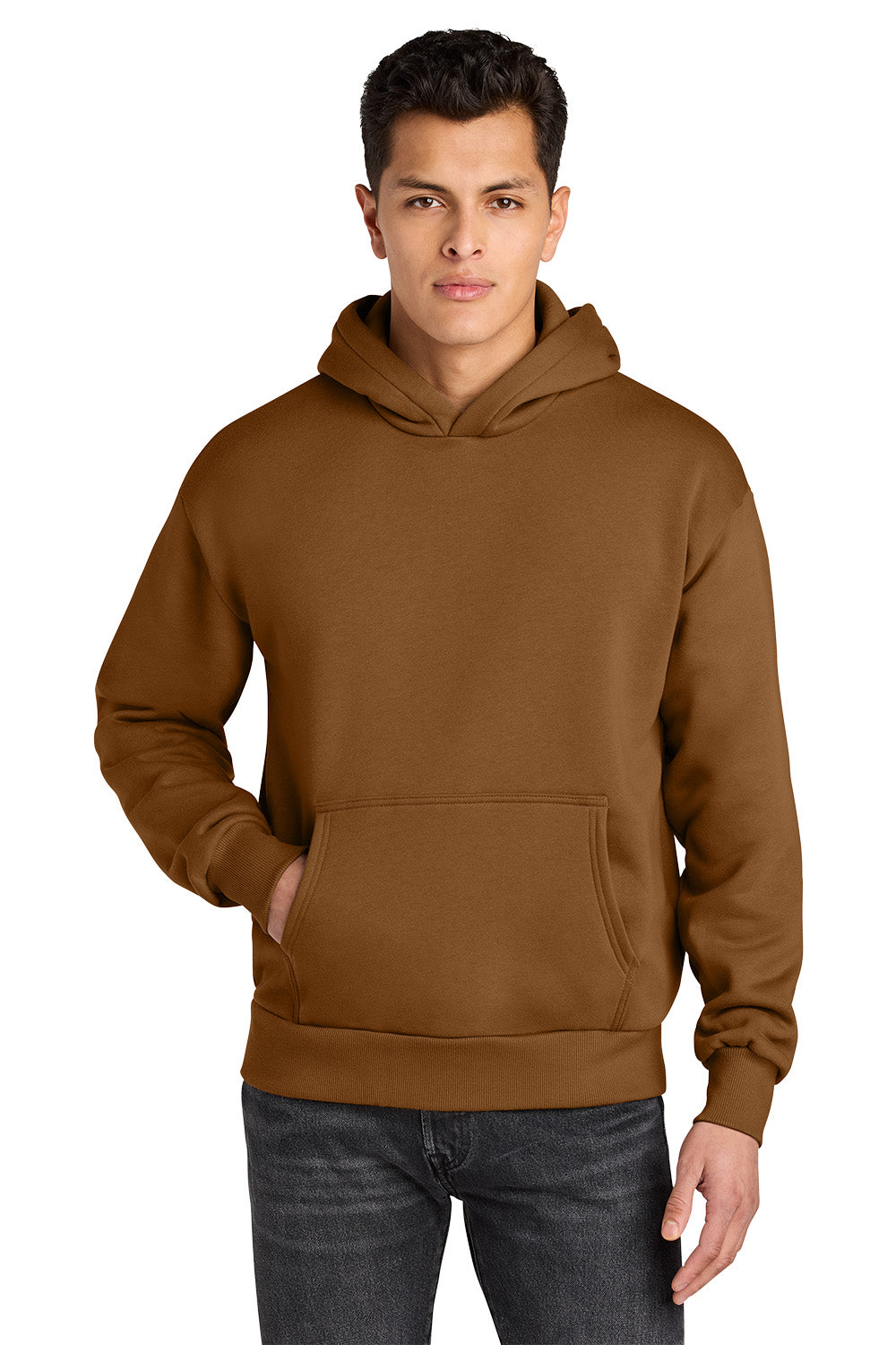 A man wearing a brown pullover hoodie with a kangaroo pocket, paired with dark gray jeans, photographed against a solid white background. Next Level Apparel® Heavyweight Hoodie, Embroidered