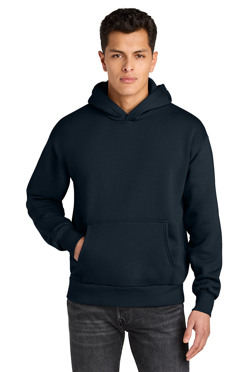 A man wearing a dark navy pullover hoodie with a front kangaroo pocket, paired with dark gray jeans, against a plain white background. Next Level Apparel® Heavyweight Hoodie, Embroidered
