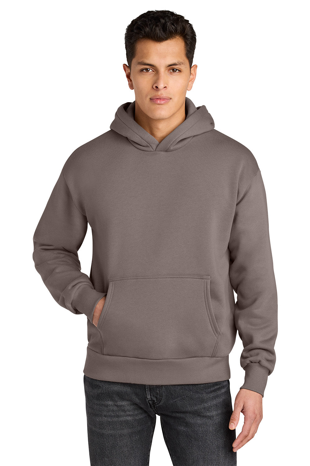A man wearing an olive green pullover hoodie with a kangaroo pocket, paired with dark gray jeans, against a plain white background. Next Level Apparel® Heavyweight Hoodie, Embroidered
