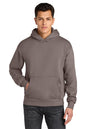 A man wearing an olive green pullover hoodie with a kangaroo pocket, paired with dark gray jeans, against a plain white background. Next Level Apparel® Heavyweight Hoodie, Embroidered