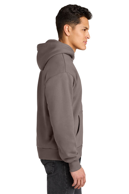 A man shown in profile wearing a solid taupe-brown pullover hoodie and dark gray jeans, photographed against a clean white background. Next Level Apparel® Heavyweight Hoodie, Embroidered